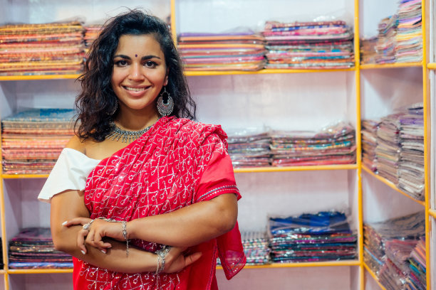 商务女士身穿红色传统纱丽和珠宝服装店老板羊绒牦牛羊毛披肩。在印度果阿，一位女售货员正在挑选布料图片下载