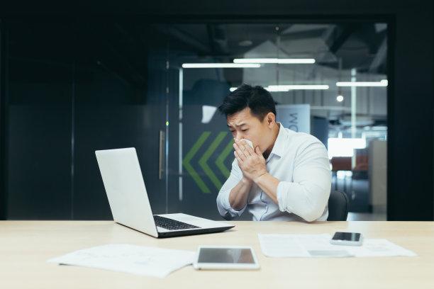 生病的人在办公室咳嗽流鼻涕，亚洲商人感冒在办公室用笔记本电脑工作图片下载