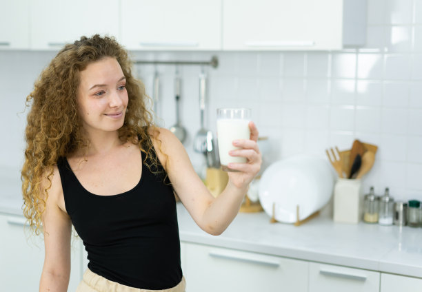 美丽的白人妇女微笑，喝牛奶，站，看牛奶杯在厨房与复制空间。美丽的白人妇女烹饪健康饮食水果或蔬菜在厨房图片下载