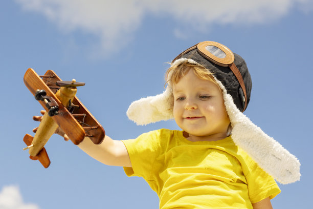 快乐的小男孩在蓝天白云的背景下玩木制玩具飞机图片下载