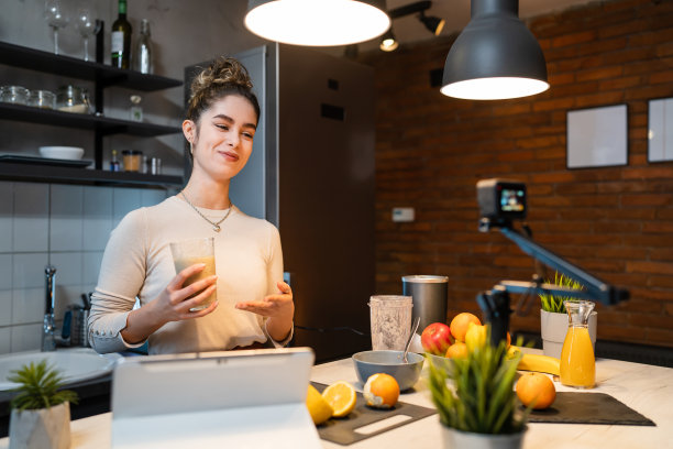 一名年轻的白人女性制作视频或作为博主在网上播放厨房里的食物准备，与她的追随者谈论食材和制作过程，解释配方图片下载
