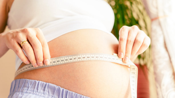 孕妇测量肚子的大小。快乐的年轻孕妇用卷尺量肚子。治疗，保健，母性观念。图片下载