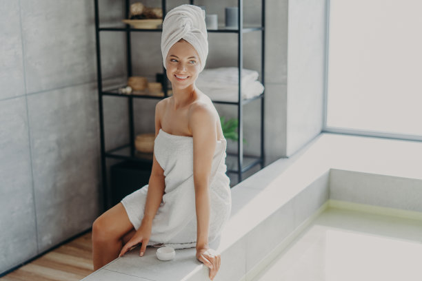美容，仪容整洁和卫生概念。放松美丽的欧洲女人与健康的皮肤微笑和看向别处，包裹在浴巾，使用化妆品霜，享受美容程序，洗澡图片下载