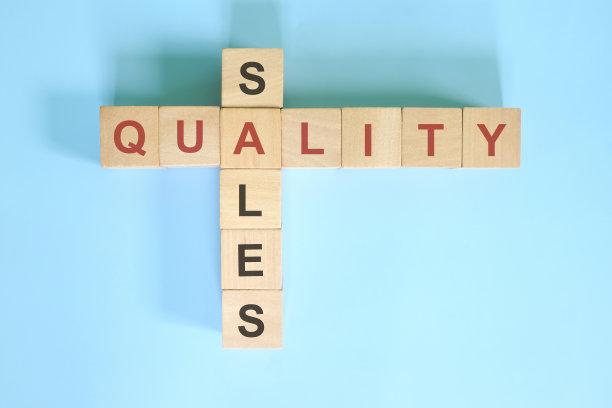 在商业中，高质量就等于更高的销售理念。木制方块纵横字谜平躺在蓝色的背景。图片下载
