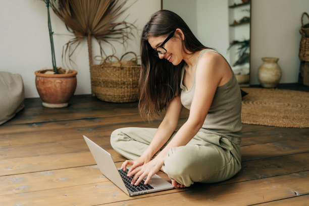 一名女生坐在木地板上使用笔记本电脑进行在线学习。图片下载