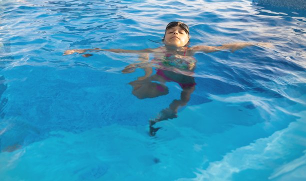 一个女孩穿着明亮的泳衣，戴着泳镜，潜入清澈透明的游泳池图片下载