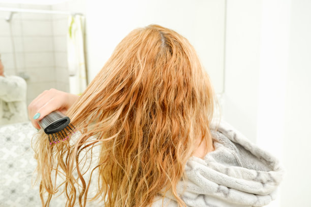 一个金发碧眼的女人在洗澡后试图用梳子梳理她乱糟糟的头发。金色，红色，梳理湿而纠结的头发。图片下载