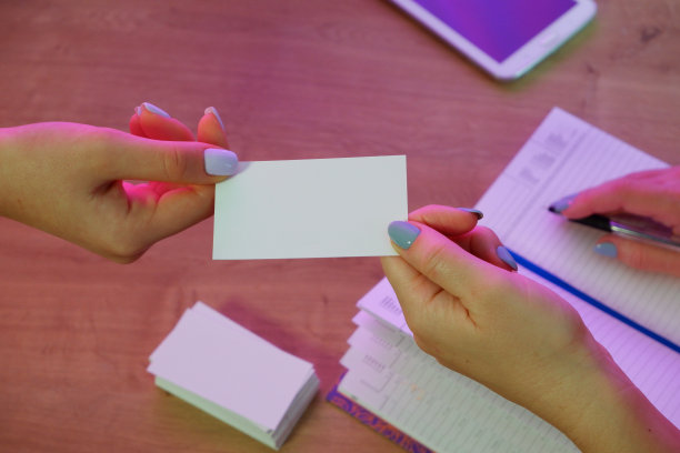 一位女士给一位客户一张名片。背景中的记事本和平板电脑放在一张木制的办公桌上。图片下载