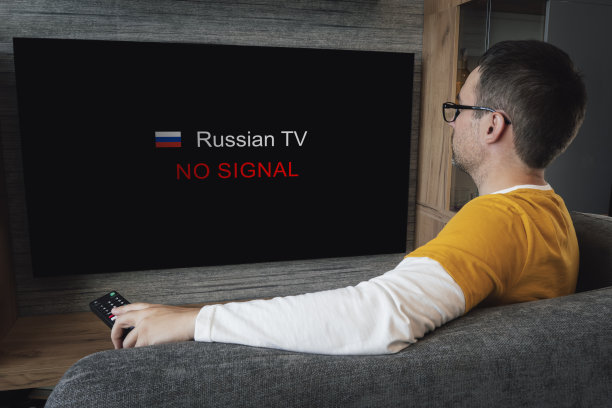 切断俄罗斯在欧洲和美国的渠道的概念。封锁俄罗斯电视广播。年轻英俊的男子在家里的沙发上看电视。图片下载
