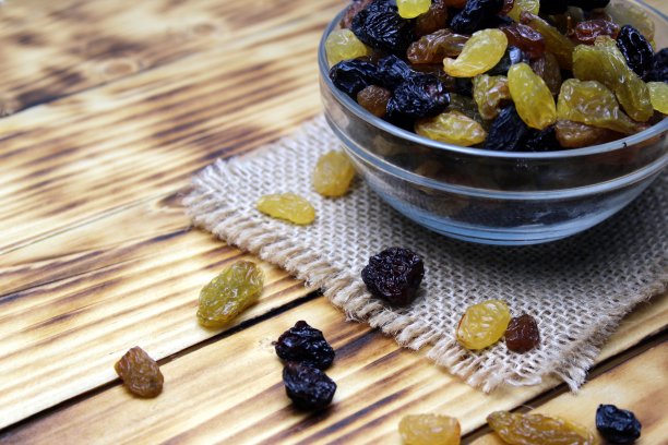 木桌上的玻璃盘子里放着几种葡萄干。图片下载