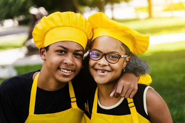 非洲儿童厨师戴着厨师帽和黄色制服微笑的特写照片。非洲少年和黑人女孩有乐趣和烹饪食物。图片下载