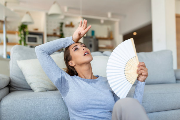 女人把头靠在沙发靠垫上感到闷热呆滞，挥挥手风扇降温，炎热的夏天没有空调空调系统的概念图片下载