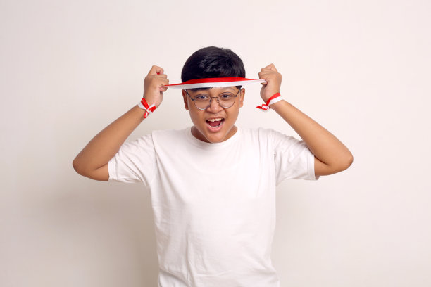 快乐的亚洲男孩站着，手里拿着红白丝带。孤立在白色背景上图片下载