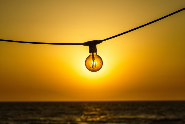 太阳能的概念。太阳通过现代节能灯丝led灯泡爱迪生风格的灯，在天空和大海的夕阳。生态学的概念。图片下载