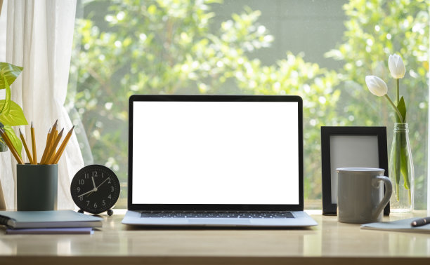 在明亮的客厅里，木桌上放着空白显示屏的笔记本电脑、咖啡杯、笔筒和相框。图片下载