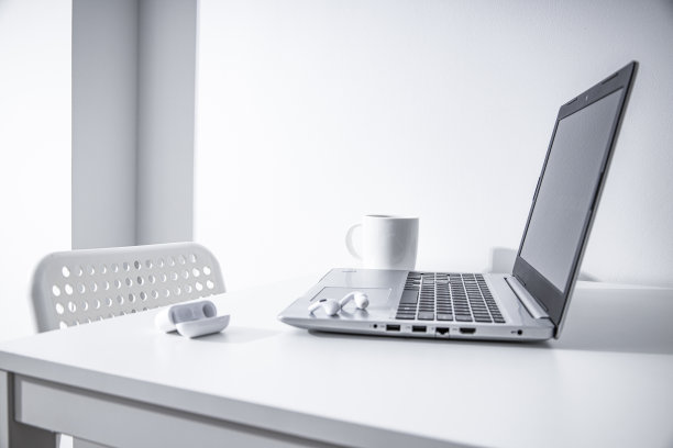 笔记本电脑，杯子，无线耳机放在白色的桌子上。自由职业者的工作场所。图片下载