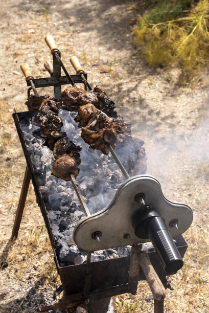 使用木炭烤架，有旋转装置和三串装着羊肉的烤串，当烟雾升起时，在覆盖着灰烬的煤炭上烹饪图片下载