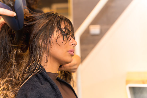 一个深色头发的女人坐在美容院用吹风机吹干她的头发图片下载