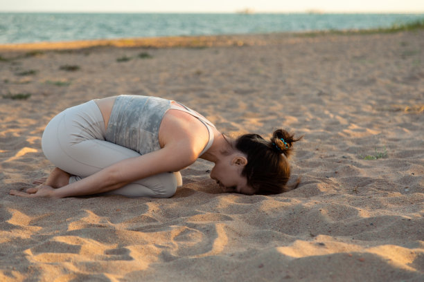 一名女子在海滩上以孩子的姿势练习瑜伽图片下载