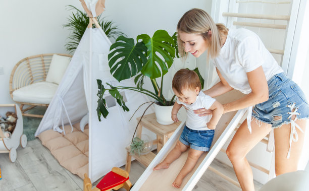 一位年轻的母亲和她的小女儿在游戏室里玩。女孩从滑梯上滚下来图片下载