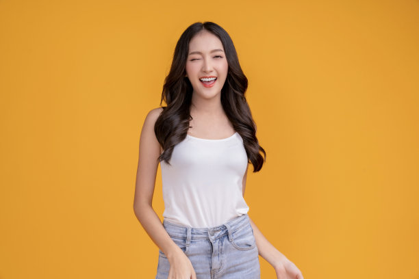 休闲幸福亚洲女性女性微笑开朗的白色t恤蓝色牛仔裤放松和平的积极思考无忧无虑的生活方式站在黄色的背景工作室拍摄素材图片