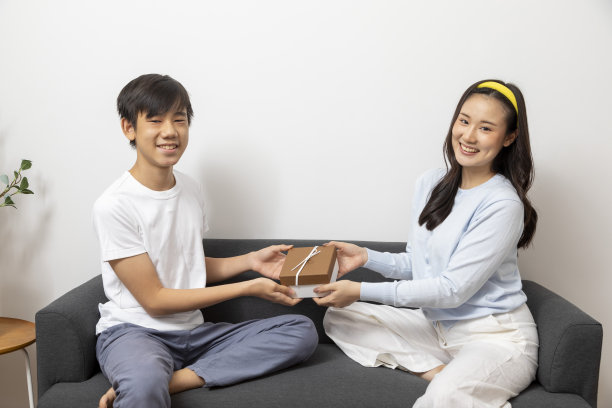 惊讶的女人从坐在客厅沙发上的男人那里收到礼物盒。图片下载