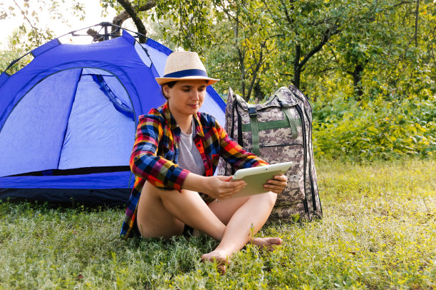 远离焦点的年轻女子在平板电脑附近露营帐篷户外环绕美丽的自然。自由职业，休假，心理健康好的姿态。远程工作。夏季旅游。的焦点图片下载