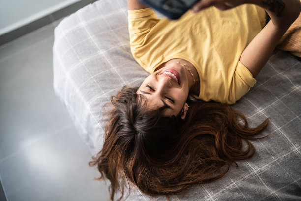 年轻女子在家里的床上使用手机图片下载