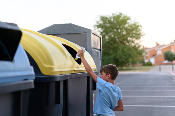 男孩把一个塑料瓶扔进黄色的容器里回收。图片下载