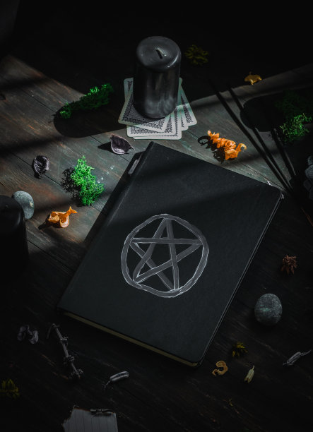 黑色皮革书与一个神奇的标志，仪式的石头，蜡烛和干花在黑色的背景。图片下载