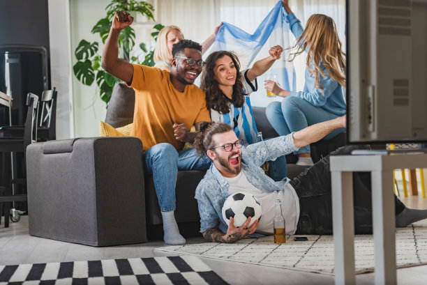 一群兴奋的多民族年轻人在家里看电视上的足球比赛图片下载