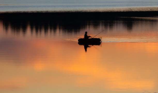 日落时分湖面上小船上渔夫的剪影图片下载
