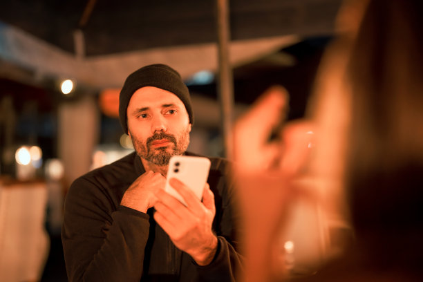 成熟的拉丁男性在酒吧或餐厅里拿着手机听别人说话图片下载