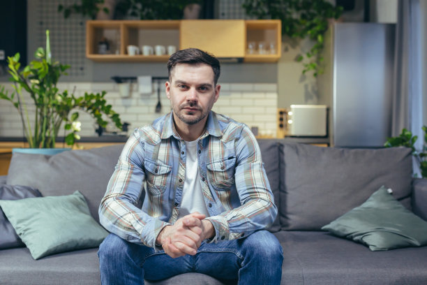 一个男人坐在家里的沙发上看着摄像机，一个搬运工正在视频通话图片下载