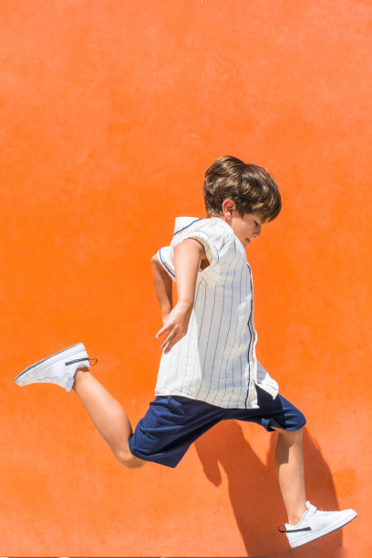 一个在橙色背景上跳跃的孩子。图片下载