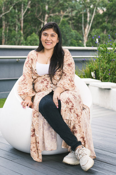 年轻女子微笑着，坐在商场的椅子上，在一片绿地上。一个哥伦比亚女孩看着镜头的肖像。图片下载