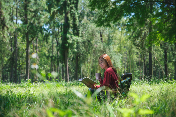 一个美丽的亚洲年轻女子的肖像读书和喝咖啡，坐在公园的露营椅上图片下载