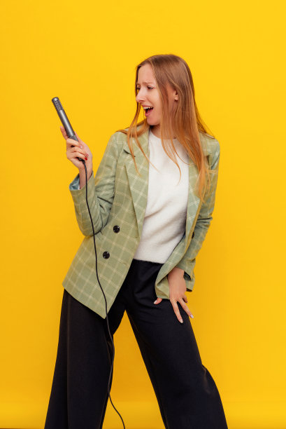 快乐的漂亮女人用麦克风唱歌的垂直镜头，呈现一个事件或有一个聚会，享受这一刻，穿着休闲的衣服站在黄色的背景。年轻的情绪化的女人图片下载