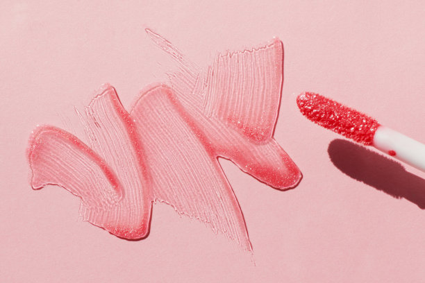 涂抹闪亮的唇彩和唇彩刷在粉红色的背景，硬阴影图片下载