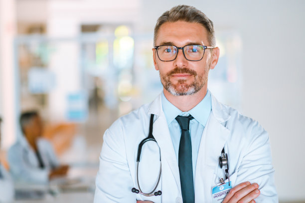 一名骄傲的医生双手交叉站在会议室里的画像，背景是医务人员。成熟的医学专业人士，自信的微笑，站在会议室图片下载