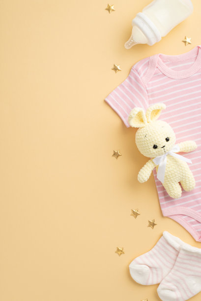 小配件的概念。俯视图垂直照片的婴儿衣服粉红色紧身衣袜子瓶子针织兔子玩具和金色的星星在孤立的粉彩米色背景图片下载