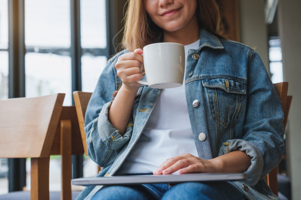 特写图片一名年轻女子拿着冰咖啡喝着，膝上放着笔记本电脑图片下载