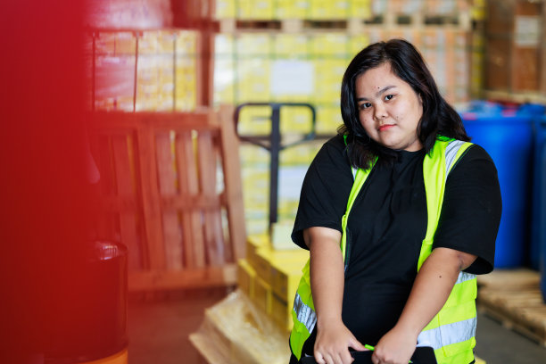 幸福微笑亚洲肥胖女仓库工人在安全背心和安全帽在仓库工厂工业。产品装在纸箱里放在货架上。加尺码女性检查产品工作图片下载