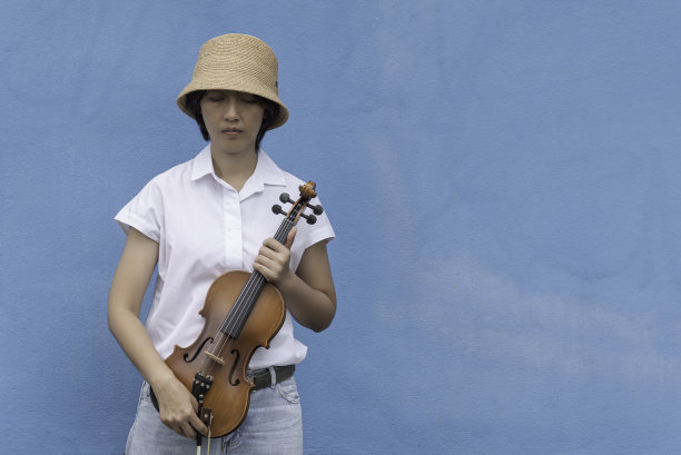 美女拿着小提琴在蓝色的墙壁上观看背景，在情感中感悟冥想。图片下载