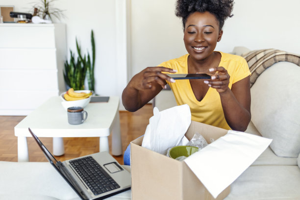 一名年轻女子正在为她在网上订购的包裹拍照。年轻快乐的女孩从网店收到了一个新包裹，拍下照片发到社交媒体上。图片下载