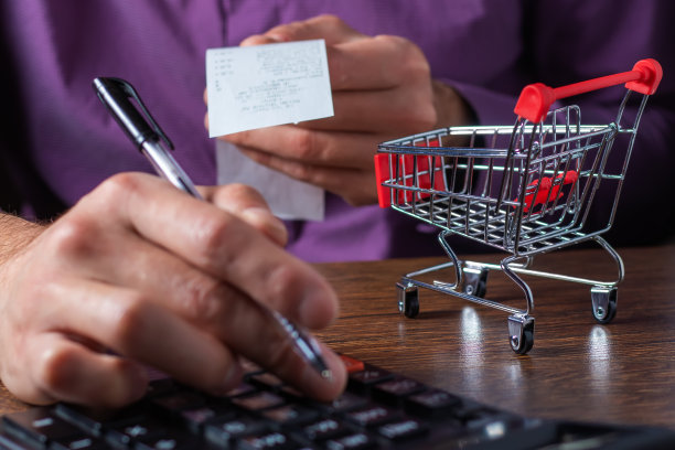 人计算预算。购物车放在桌子上，上面有计算器和纸张。手拿销售收据。图片下载