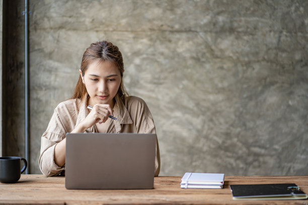 美丽的雄心勃勃的亚洲女员工在家工作。女孩用笔记本电脑微笑如梦学生们感到写文章的灵感。图片下载