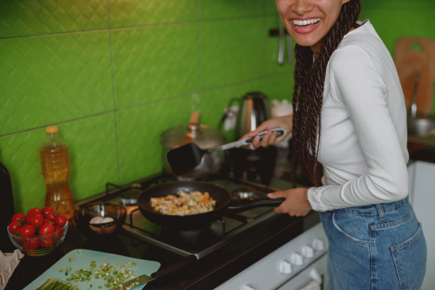特写快乐的年轻女性家庭主妇与辫子大笑和烹饪健康的饭菜图片下载