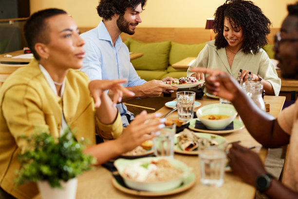 一群来自不同文化背景的朋友坐在餐厅里，吃着晚餐，聊天。图片下载