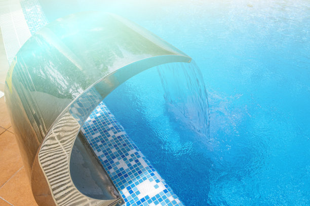 池的一面。夏季阳光明媚的日子里，空旷的户外游泳池和瀑布喷气机。海滨度假和酒店度假的概念。倒影在湛蓝清澈的海水池中图片下载